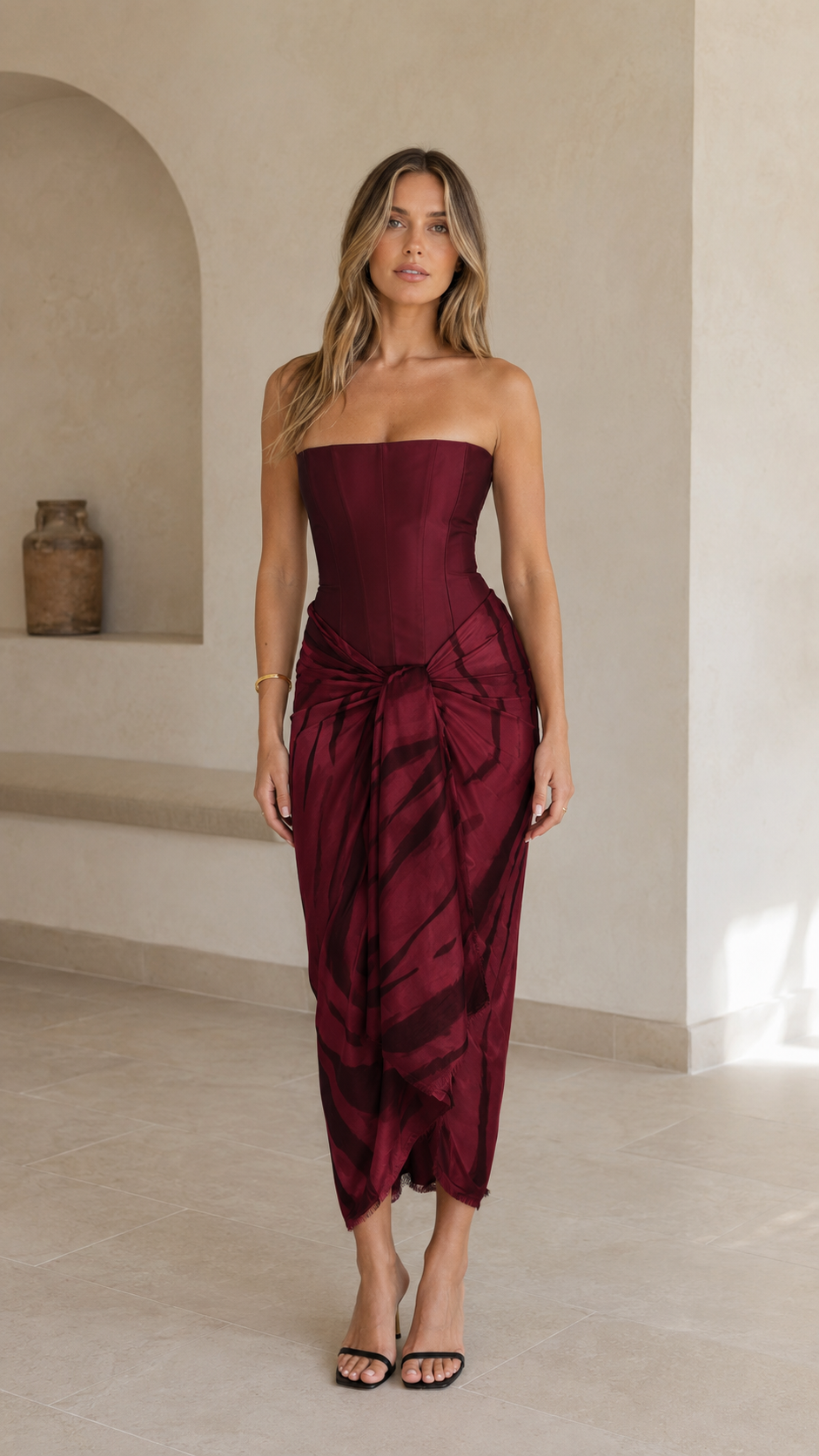 Front view of a strapless burgundy corset midi dress with a dark abstract draped skirt