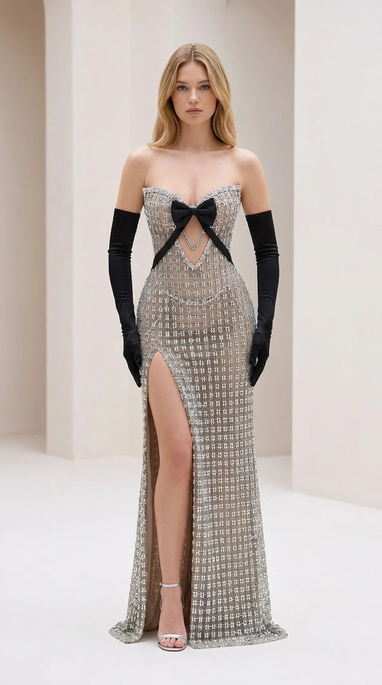 Front view of model wearing silver crystal strapless evening gown with black bow and high slit