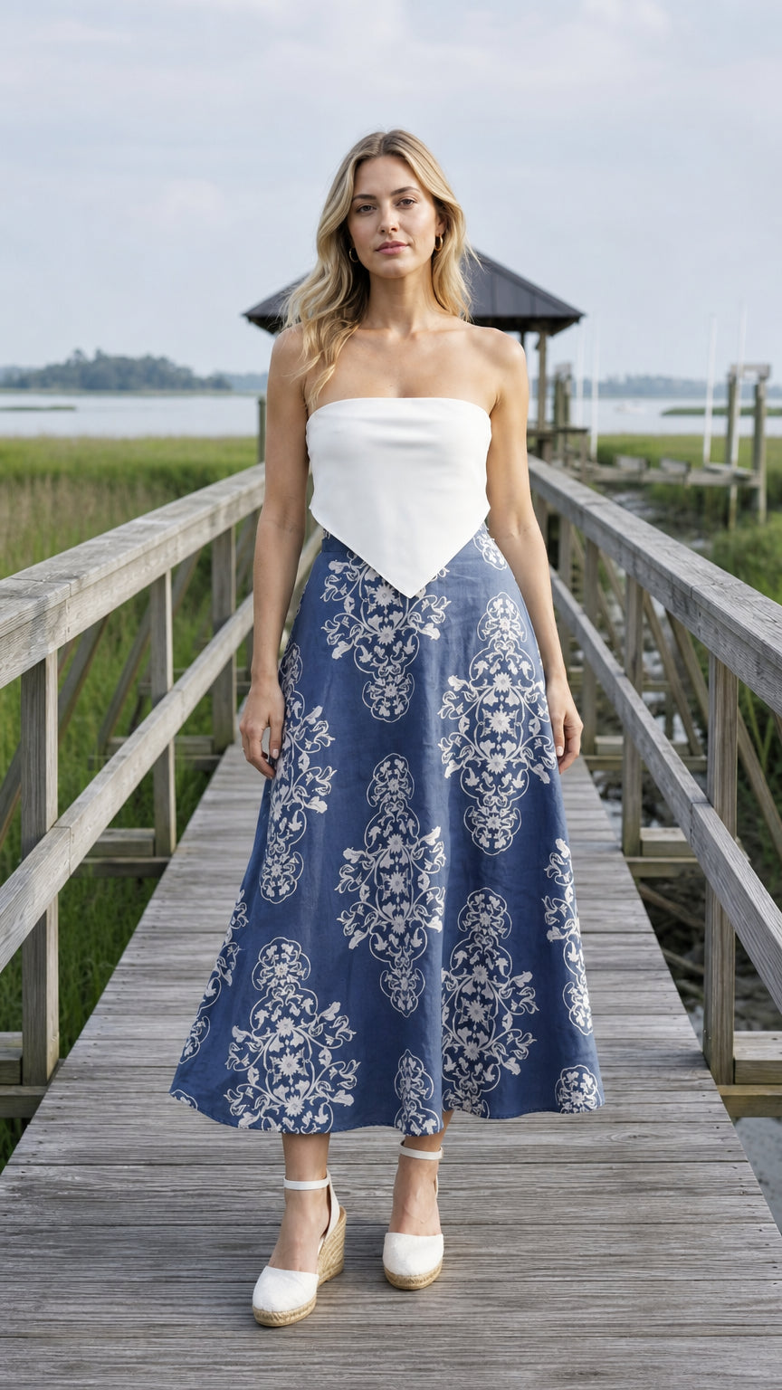 Front view of blue floral midi skirt paired with white top on wooden dock