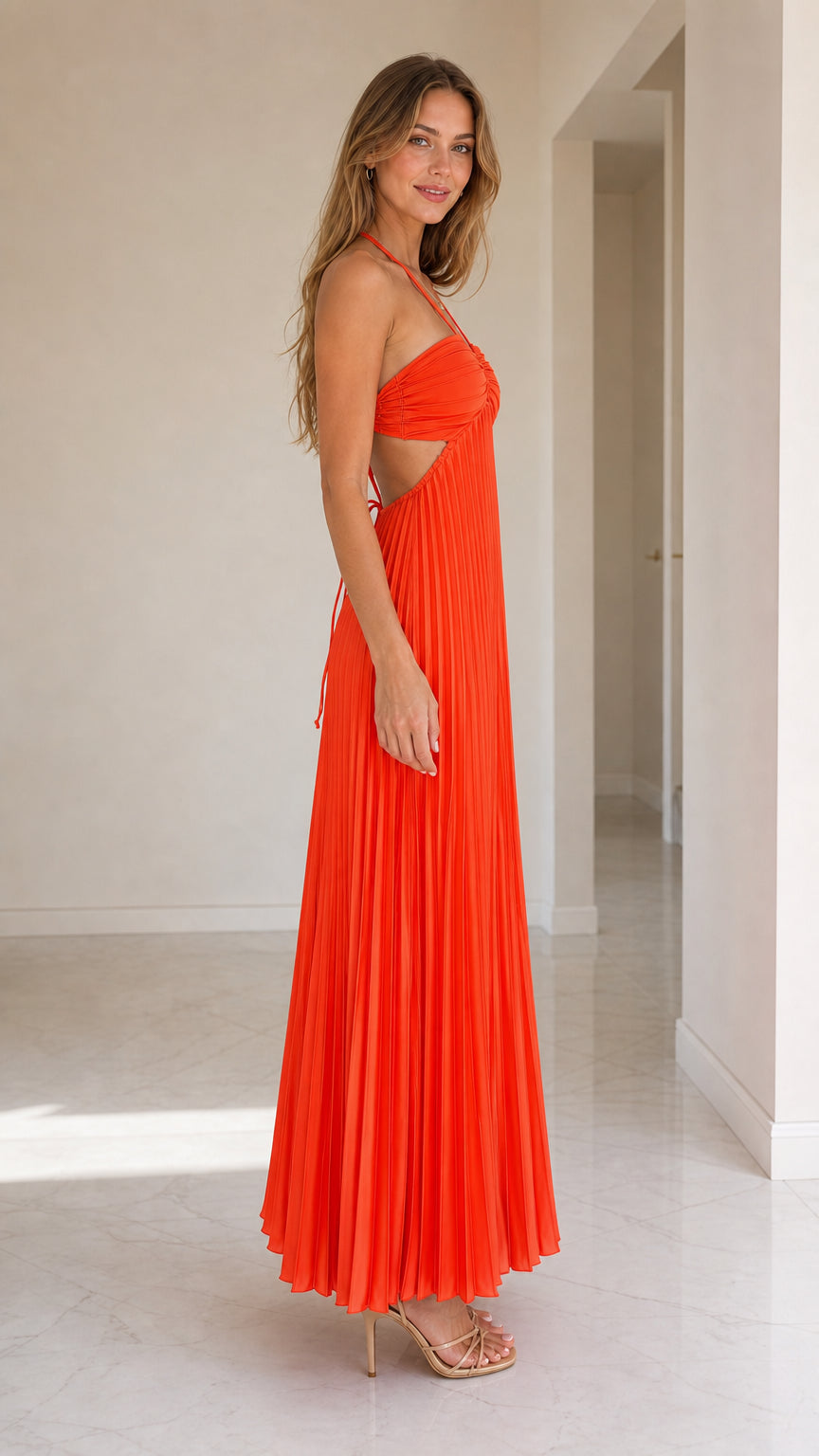 Side profile of model in orange pleated maxi dress with cut-outs