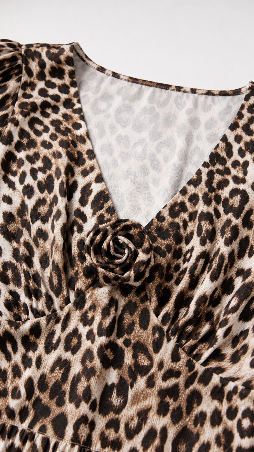Close-up detail of V-neckline and rosette accent on leopard print fabric
