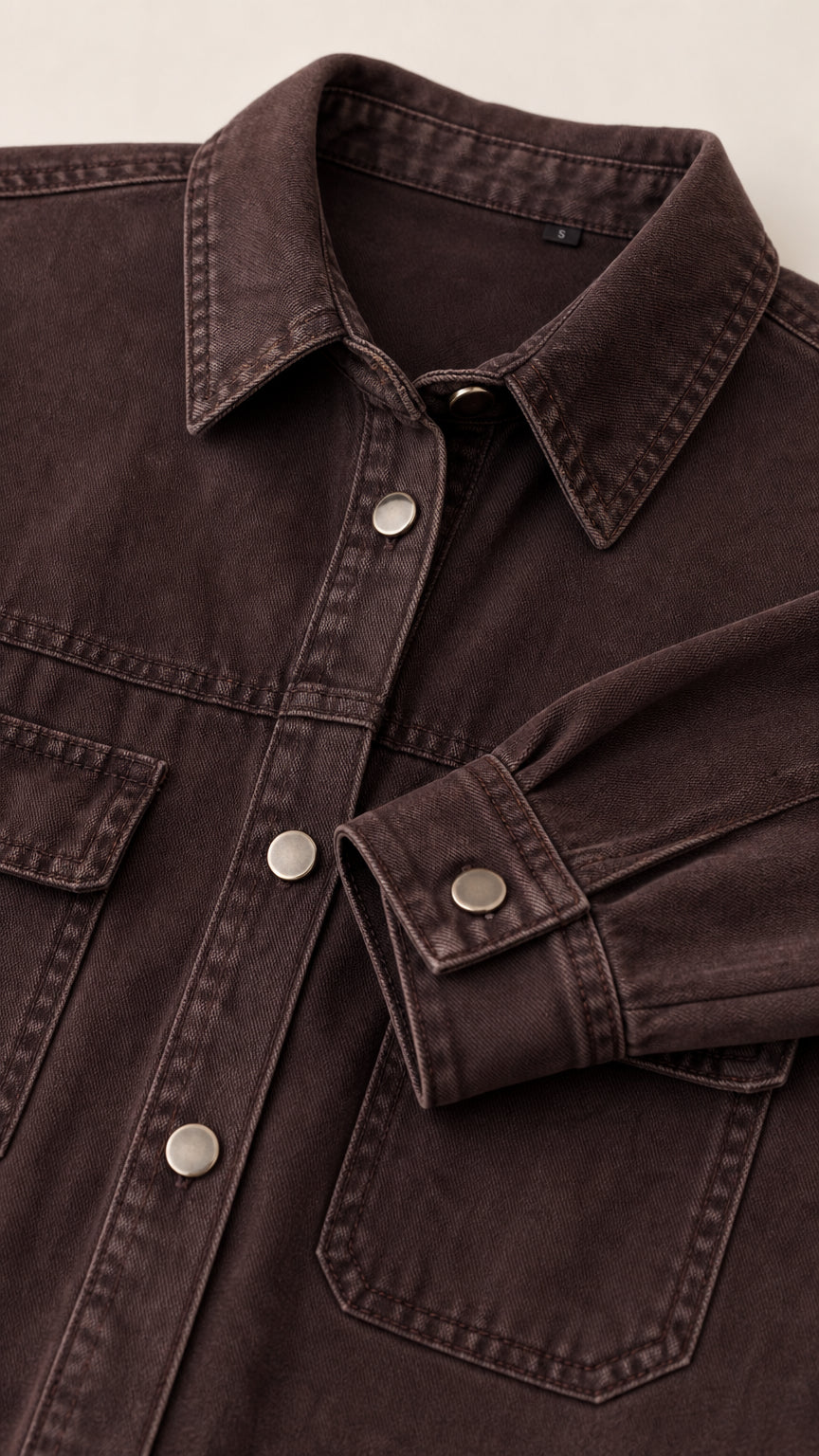 Close-up detail of collar, snap buttons, and chest pocket on brown denim dress