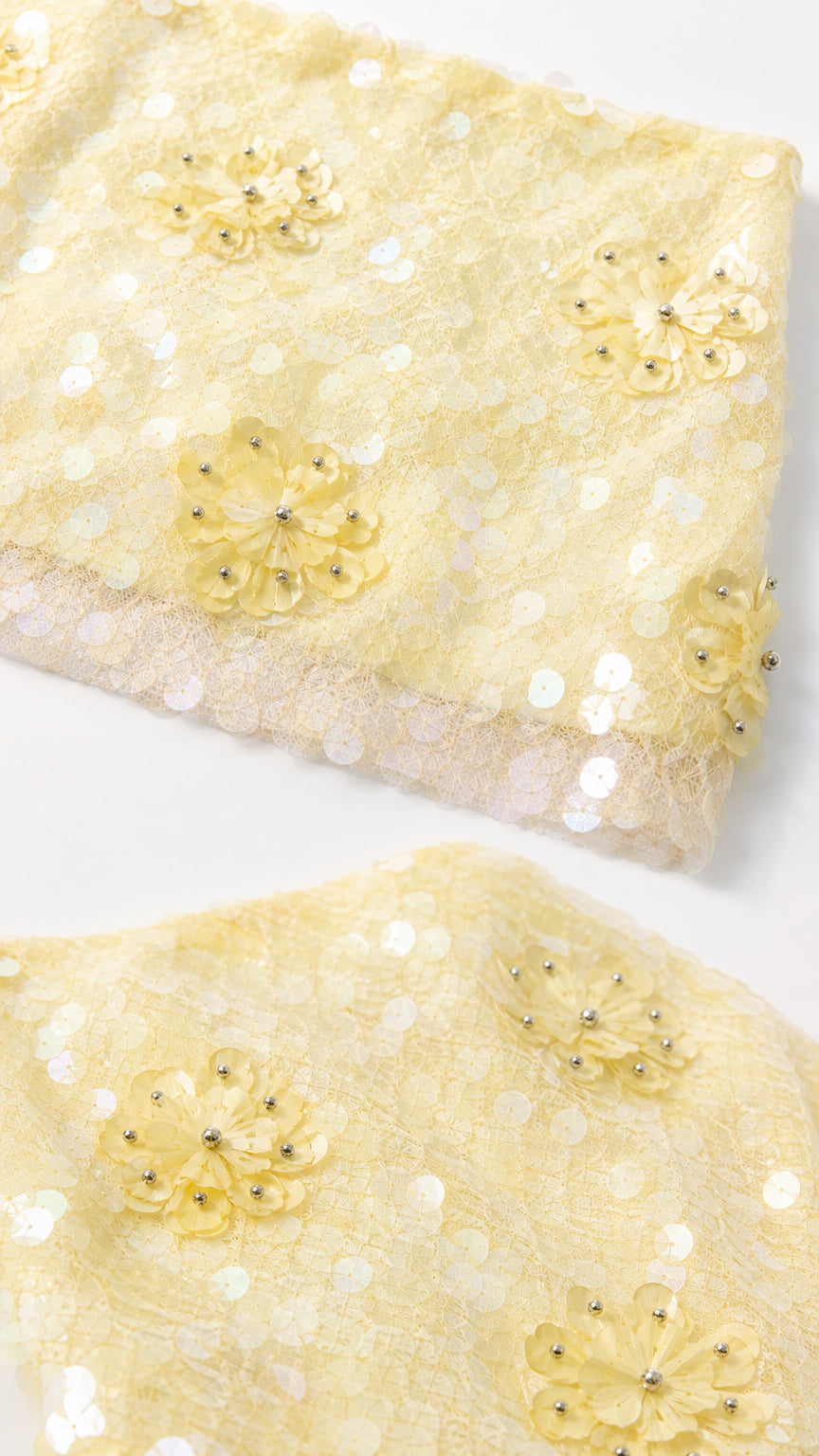 Close-up detail of yellow sequin fabric and floral appliqués