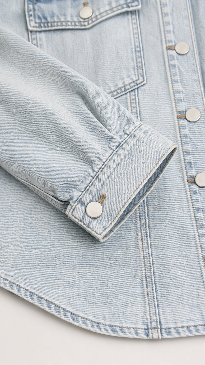 Close-up detail of light blue denim shirt jacket sleeve cuff and pocket