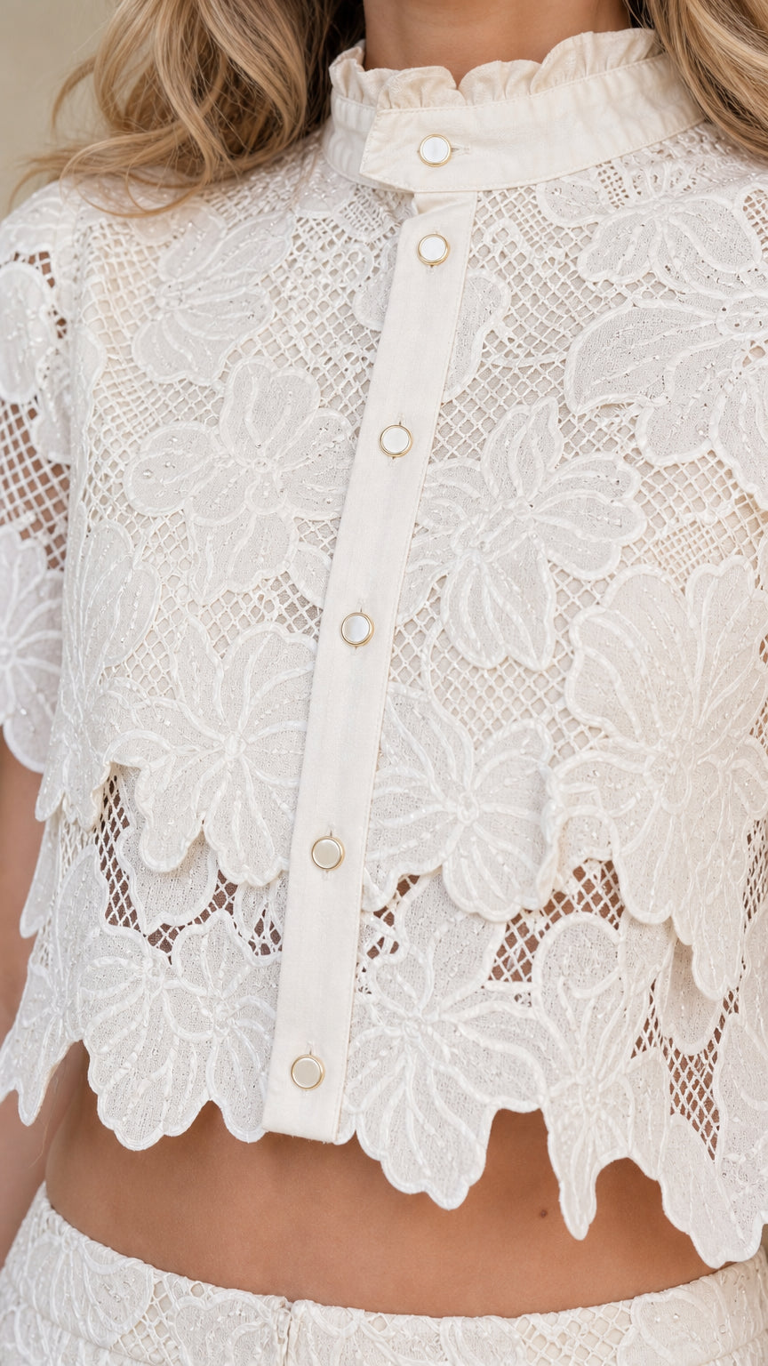 Close-up detail of white lace top with buttons and scalloped hem