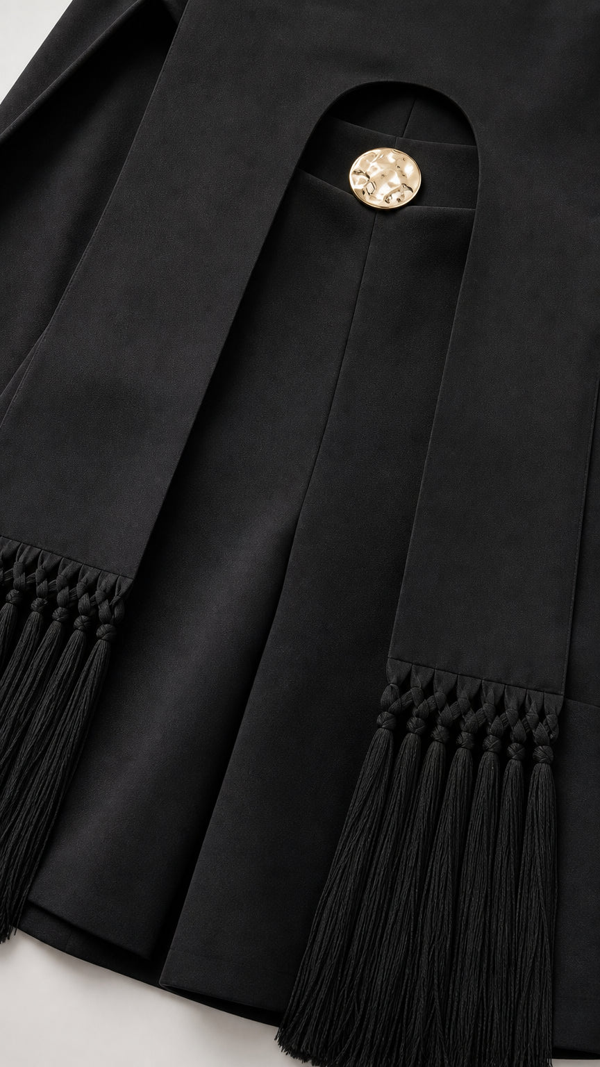 Close-up of black fabric, gold button detail, and tassel fringe hem