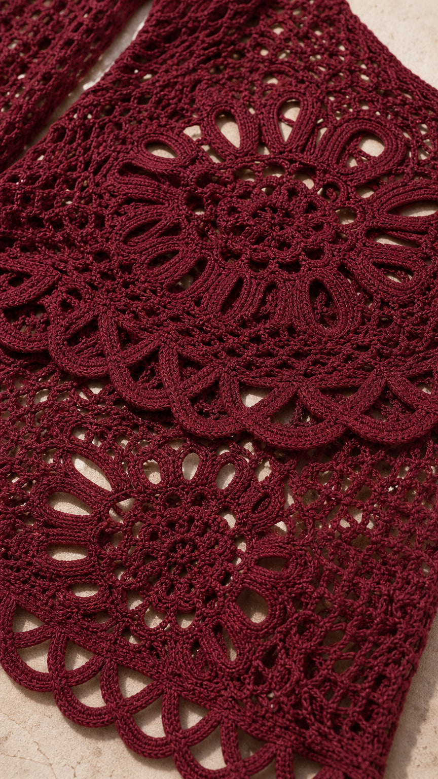 Closeup detail of burgundy open-knit crochet fabric and scalloped hem