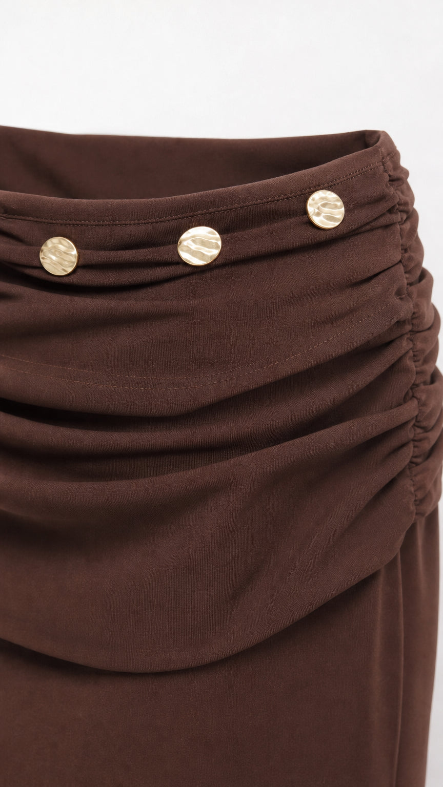 Close-up detail of ruched waistband and metallic buttons on brown mini skirt