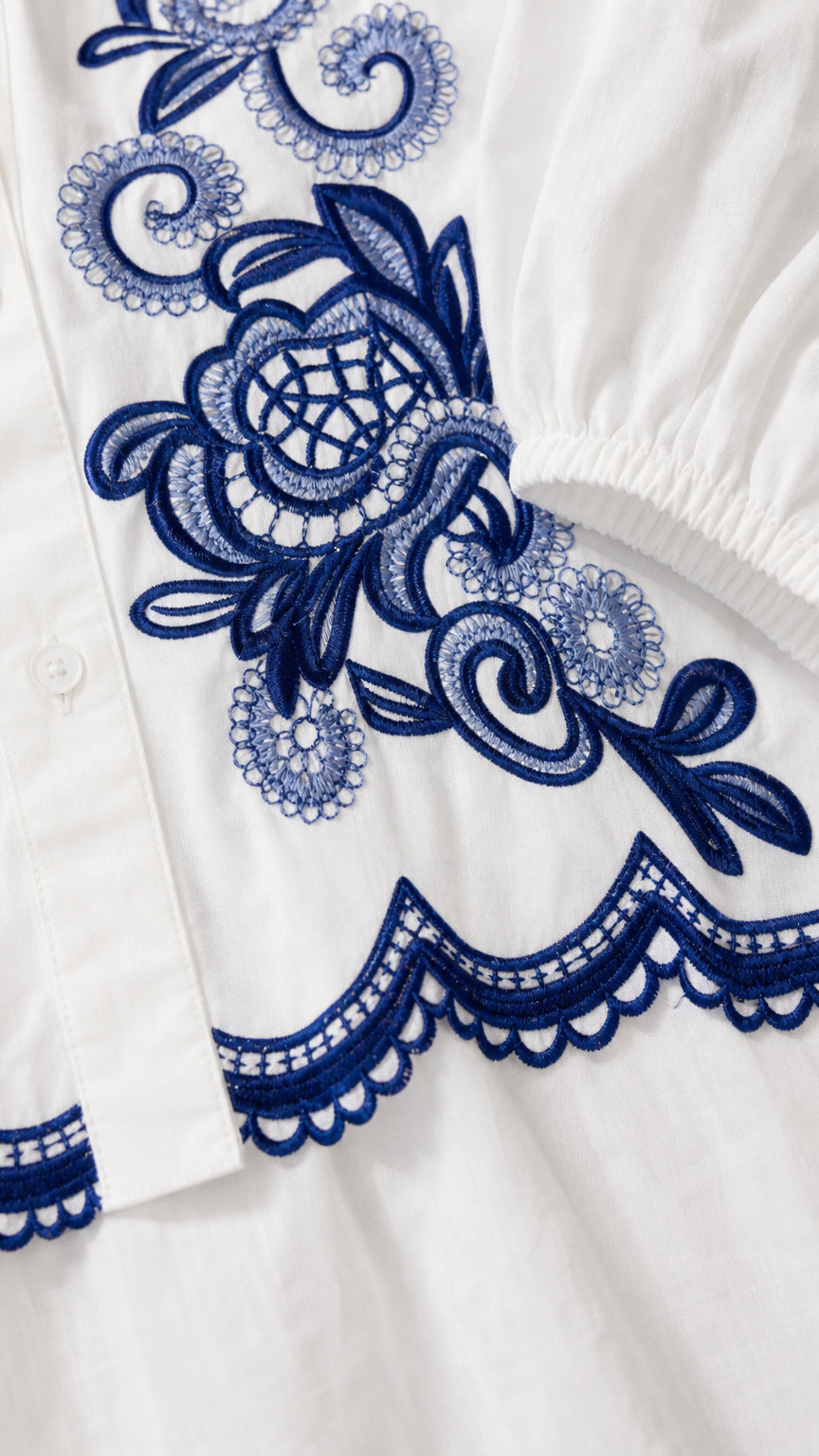 Close-up detail of blue embroidery and scalloped hem on white fabric