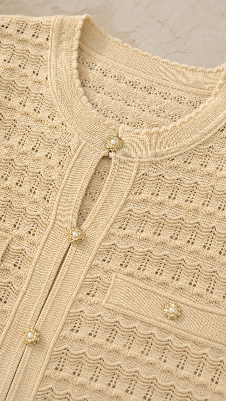 Close-up detail of beige knit top featuring pearl buttons and textured pattern