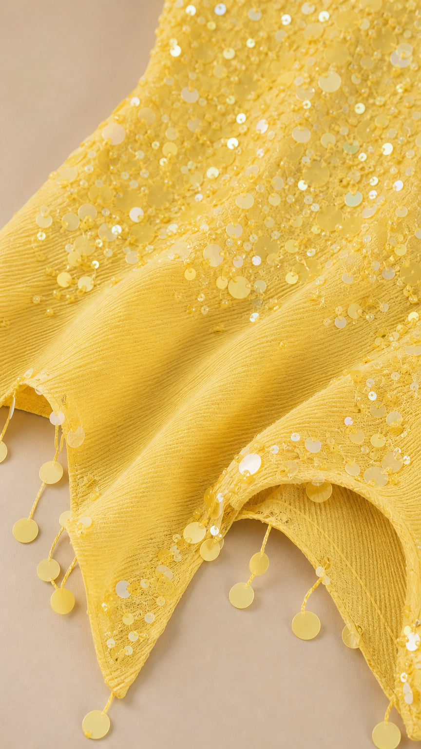 Close-up detail of yellow sequin textured fabric and coin hem accents