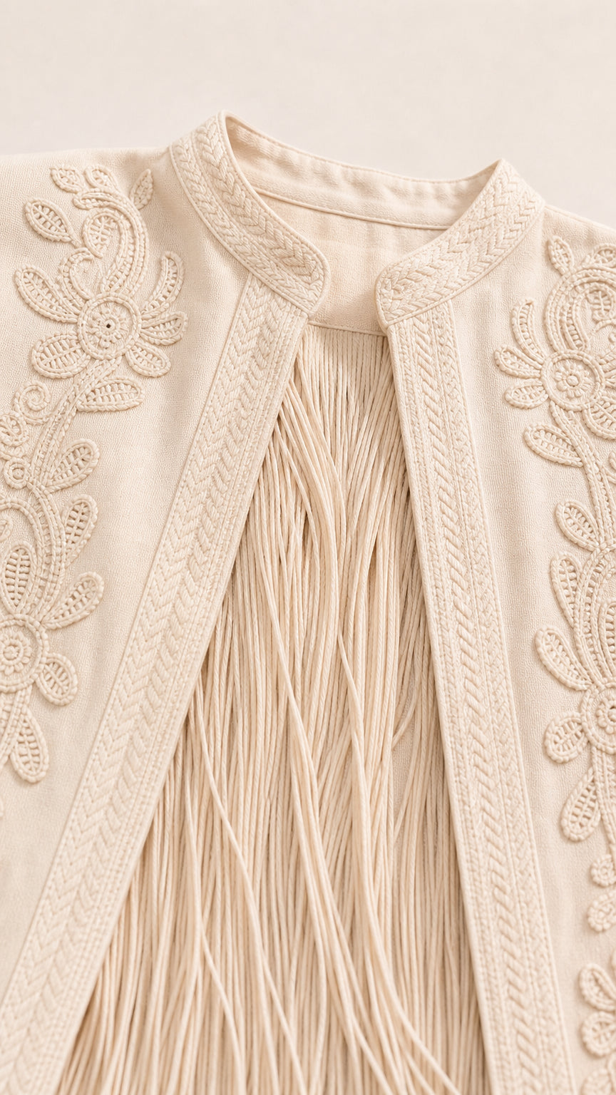 Close-up of embroidery and fringe details on beige jacket
