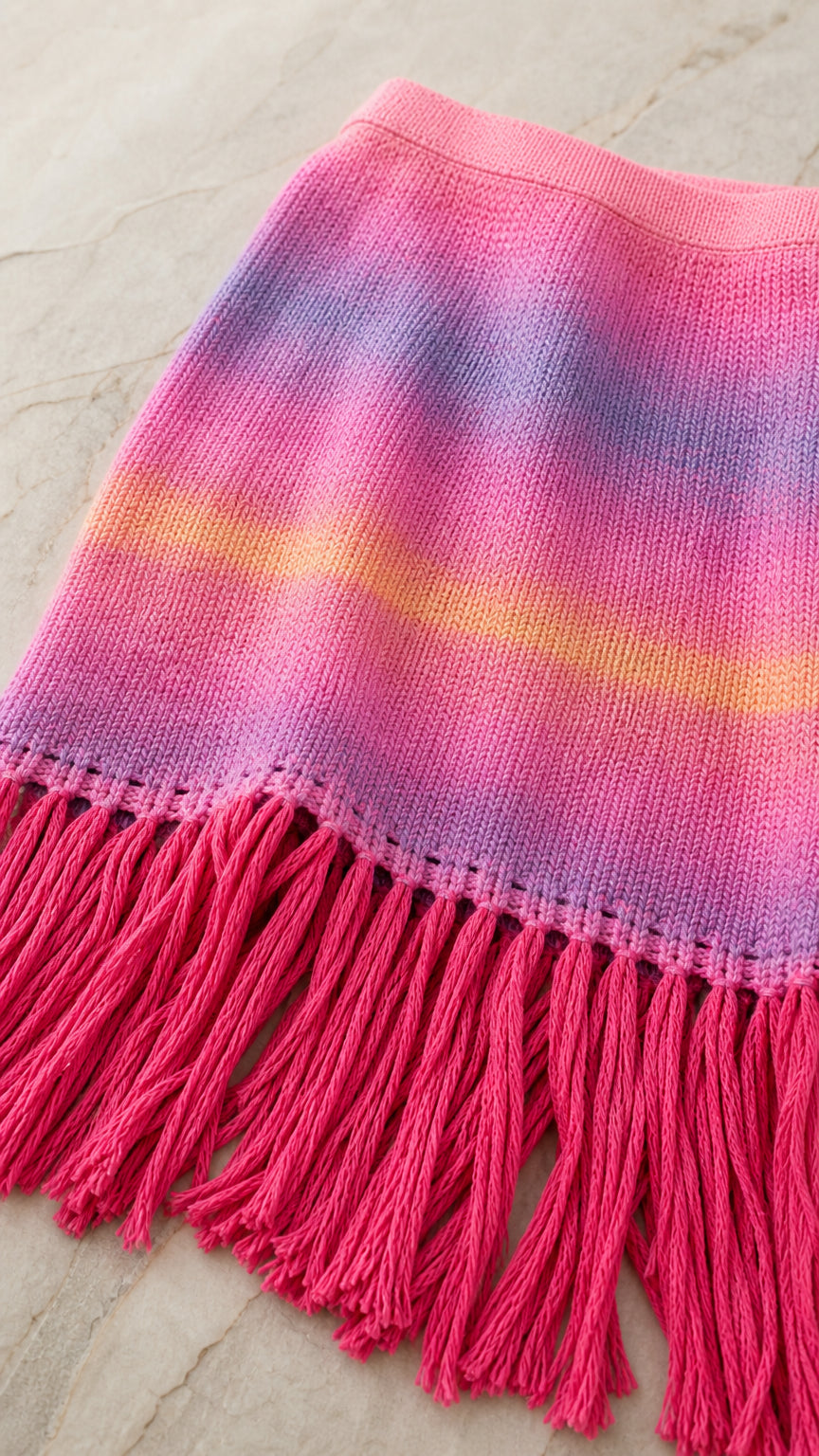 Close-up detail of the pink ombre striped knit fabric and fringe hem