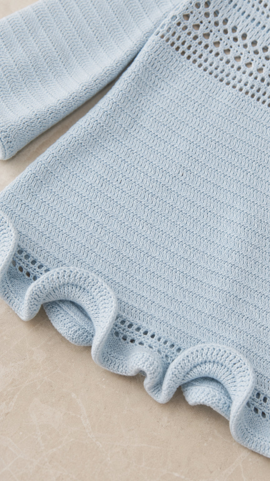 Close-up detail of the open-knit sleeve and ruffled hem in light blue