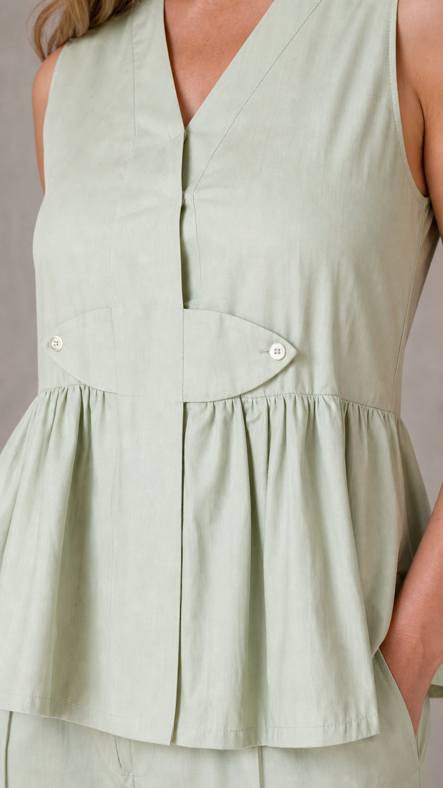 Close-up detail of sage green peplum top with buttons and wrapped waist
