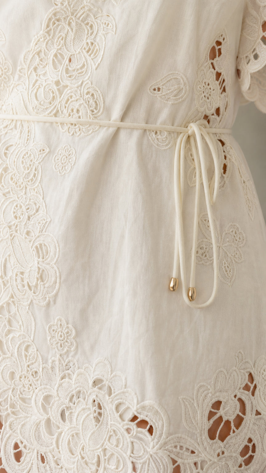 Close-up of white dress embroidery and self-tie belt detail
