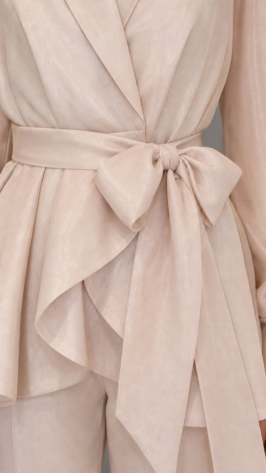 Close-up detail of self-tie bow and wrap peplum hem in beige