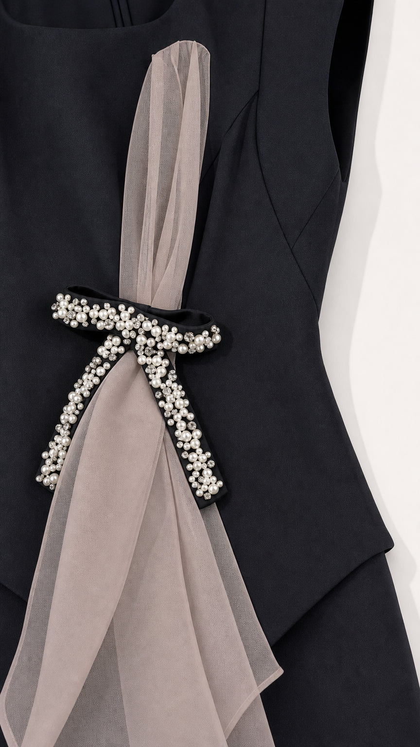 Close-up detail of pearl-embellished bow and organza sash on black dress