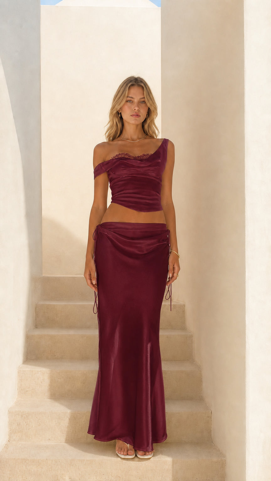 Woman wearing burgundy satin asymmetrical crop top and midi skirt set