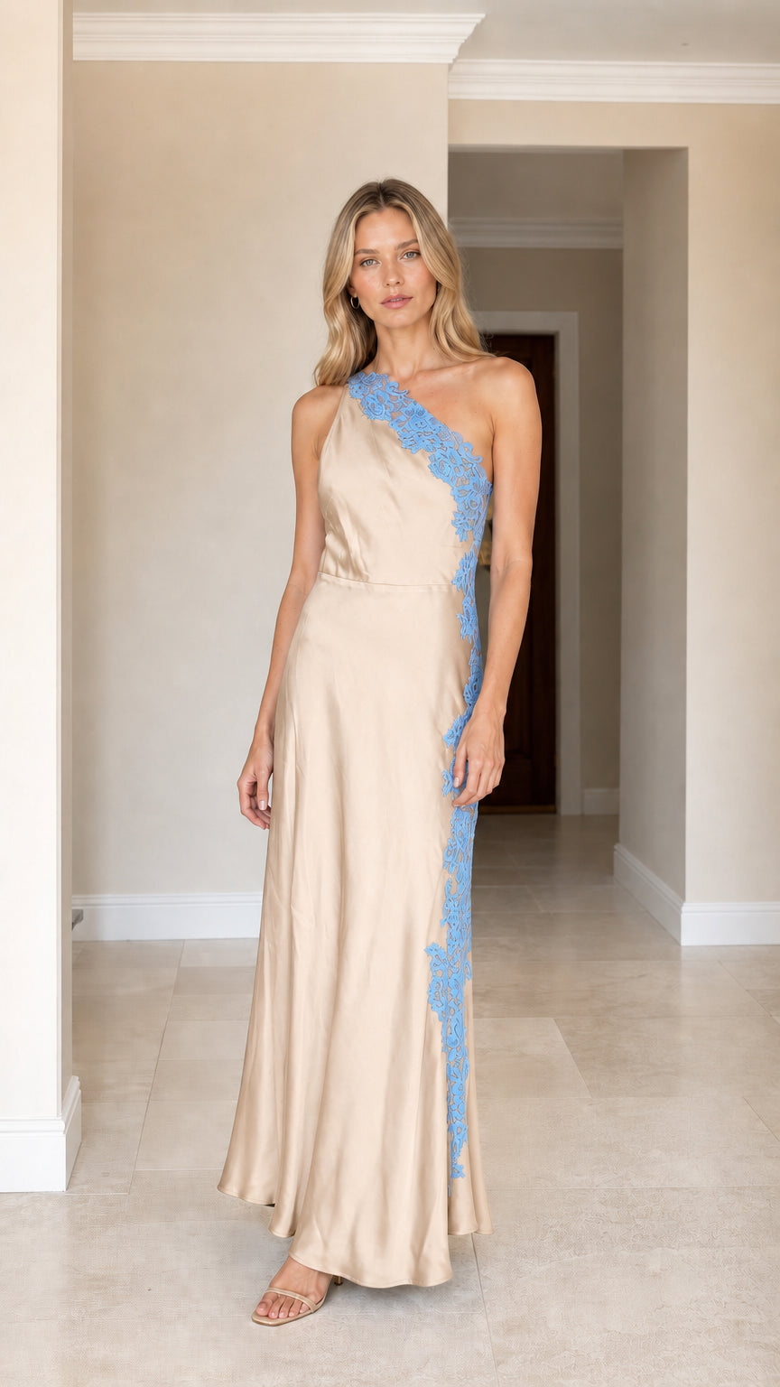 Front view of woman wearing champagne one-shoulder satin maxi dress with blue lace applique