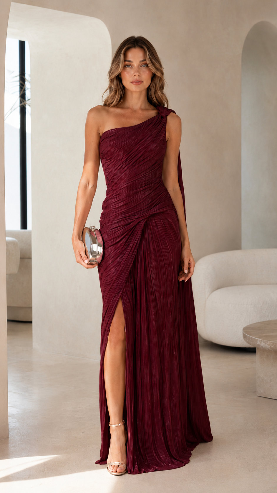 Model wearing a burgundy one-shoulder pleated maxi dress with metallic clutch